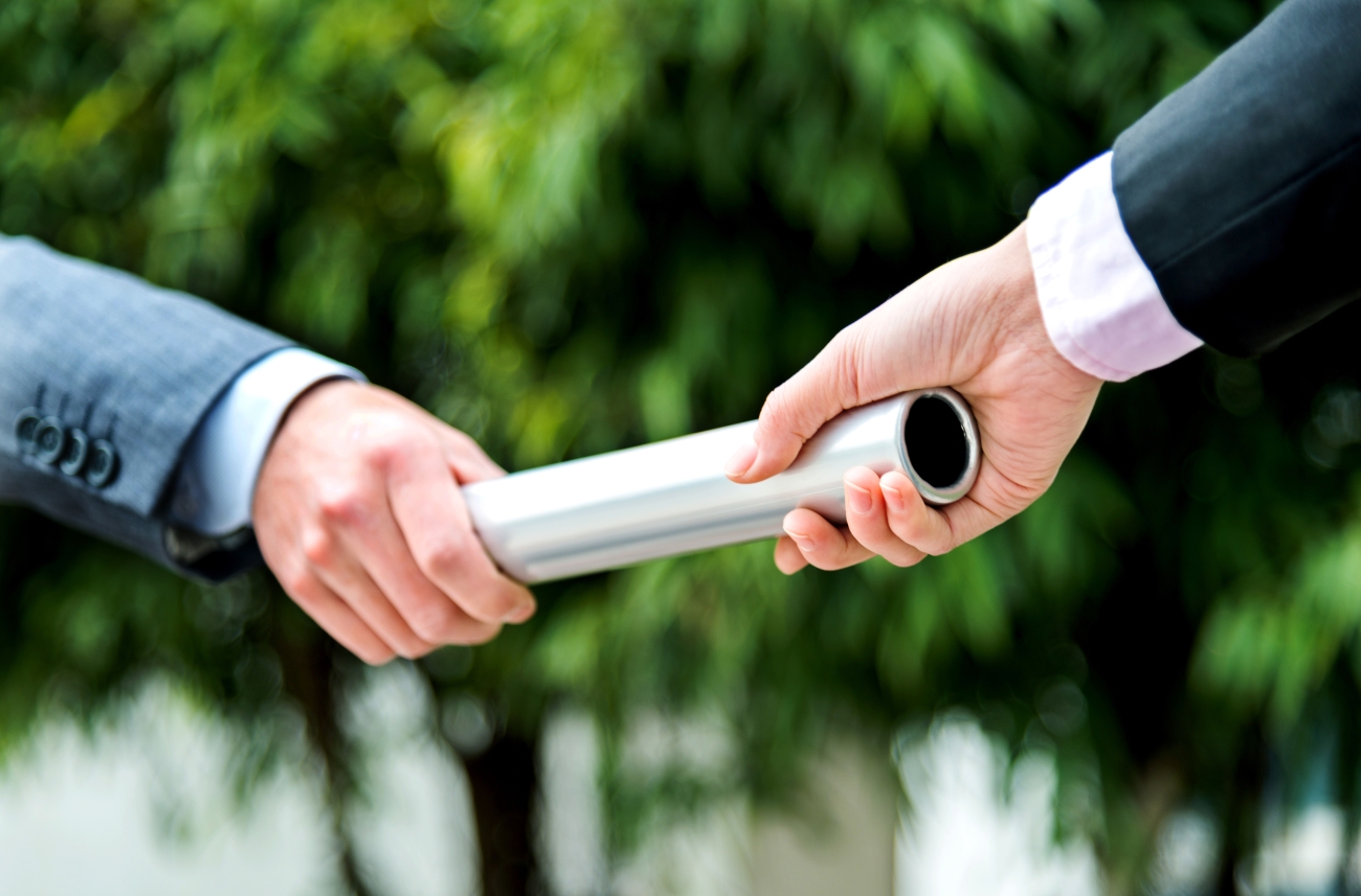 Person passing a baton to another person.